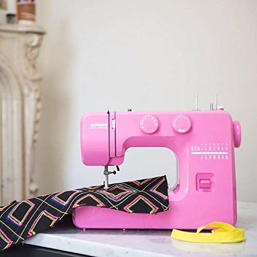 Pink sewing machine stitching colorful fabric on table