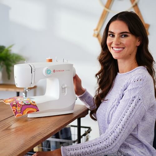 Woman smiling while using a sewing machine at a table.